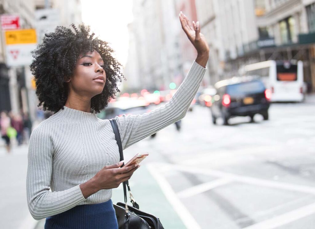 Livery Insurance - Young Woman Hailing Her Ride Share Car Service in a Bustling City on a Sunny Day